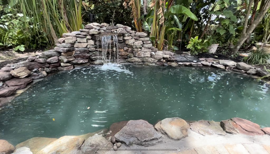 Peaceful koi pond with a cascading waterfall surrounded by natural stones and lush greenery.